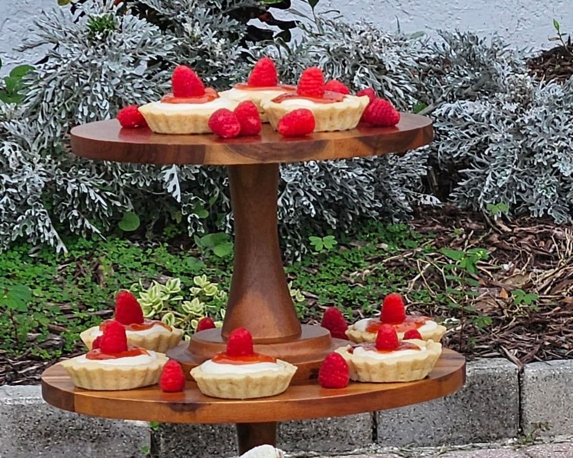 Tartlets topped with fresh raspberries on a wooden tiered stand