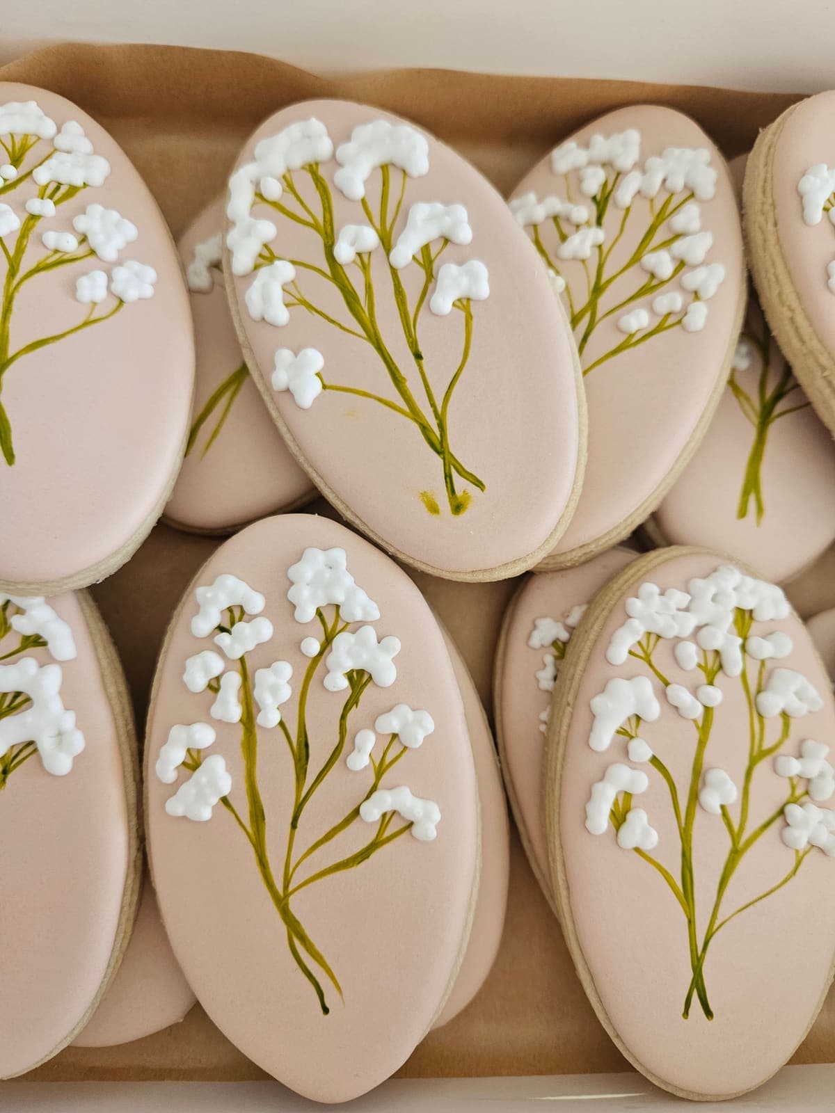 Oval sugar cookies in blush royal icing with hand piped baby's breath