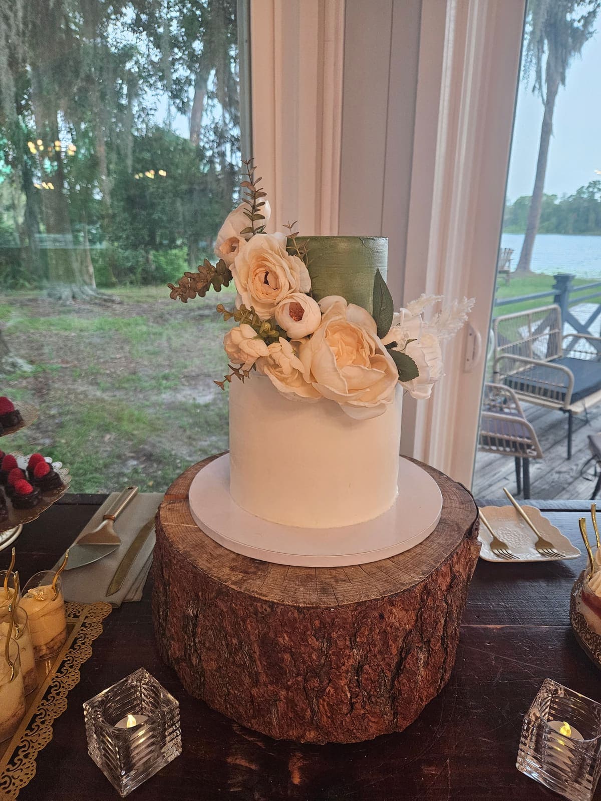 One tier white cake with a sage green top and white flowers, displayed on a wood slice