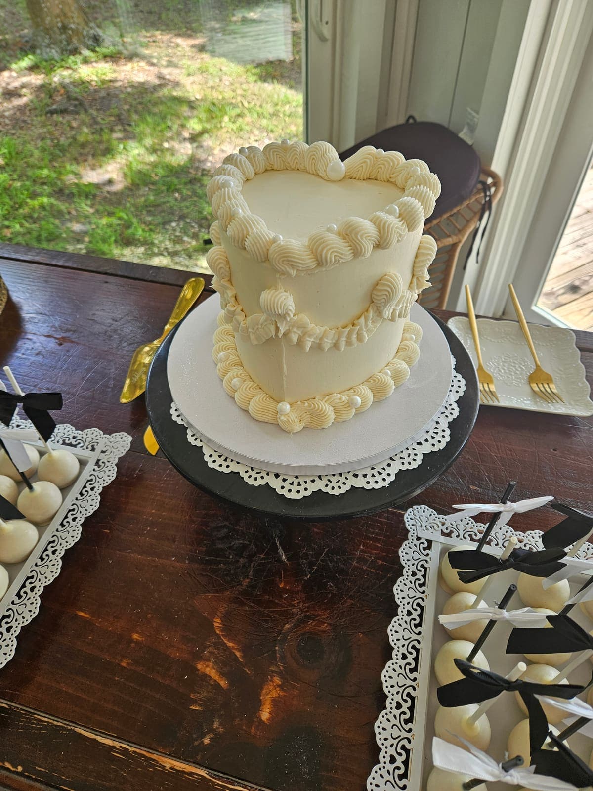 Heart shaped cake with vintage piped buttercream borders, beside cake pops tied with black and white bows