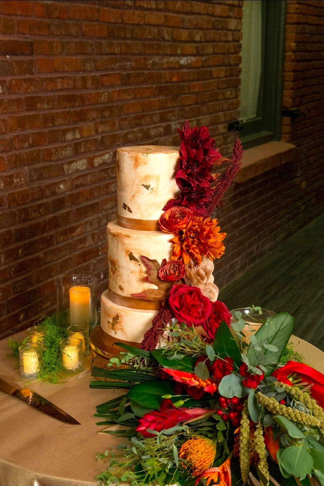 Three tier marbled wedding cake with gold accents and a cascade of red and orange flowers