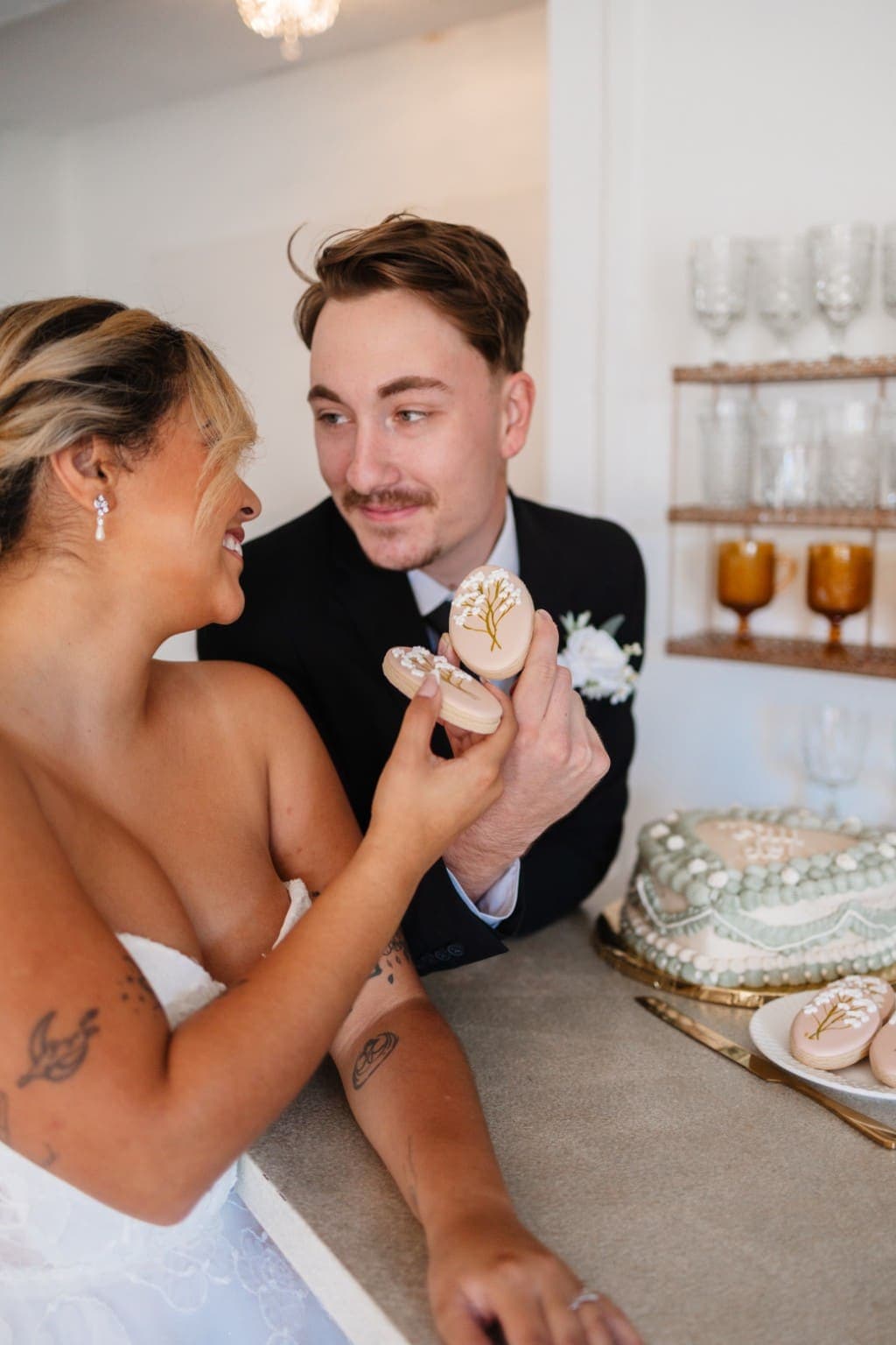 A couple holding blush sugar cookies piped with baby's breath, beside a heart shaped cake