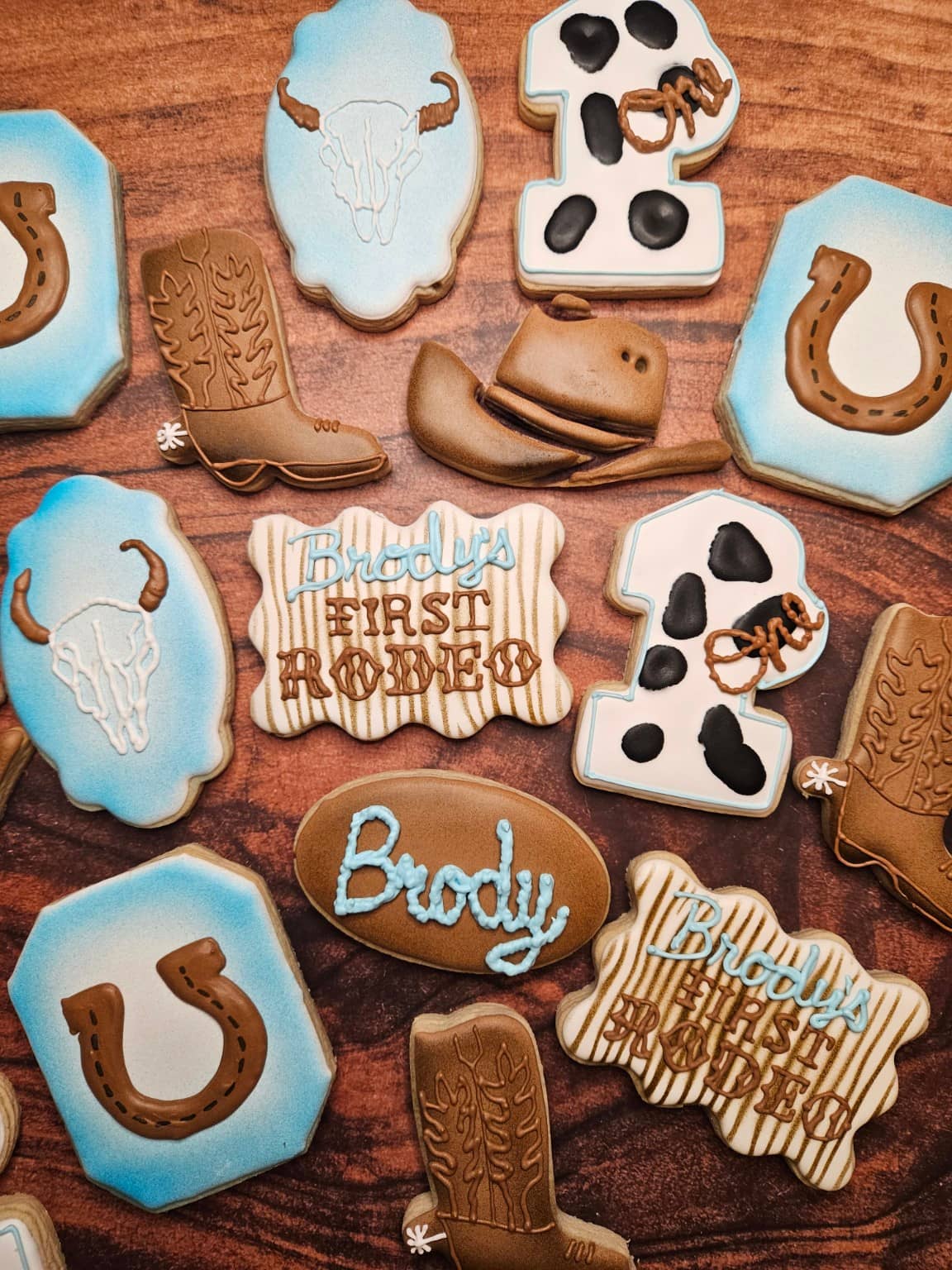 Custom first birthday cookies in a rodeo theme with boots, horseshoes and hats in blue and brown icing